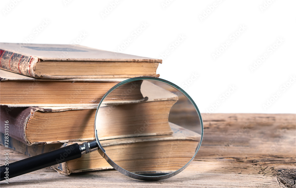 Old books and magnifying glass on textured wooden surface isolated on white background