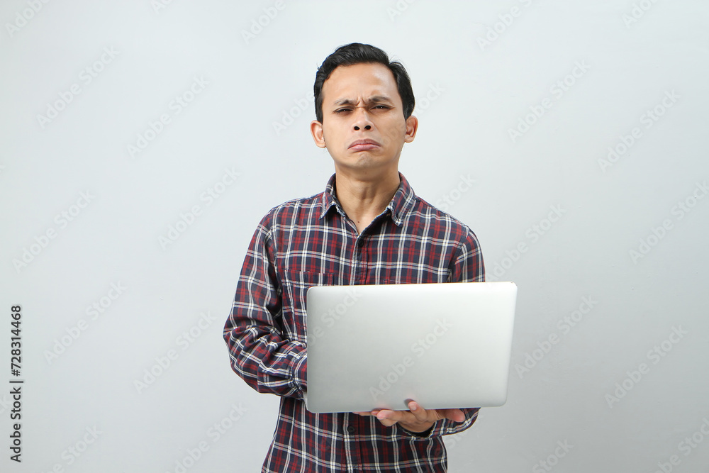 sad crying expression of asian indonesian man holding laptop computer on isolated background sad crying expression of asian indonesian man holding laptop computer on isolated background