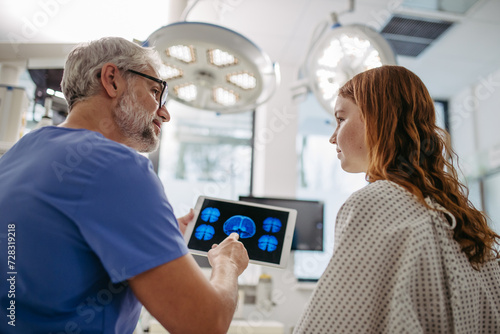 Doctor showing teenage patient MRI scan on tablet  discussing test result in emergency room.