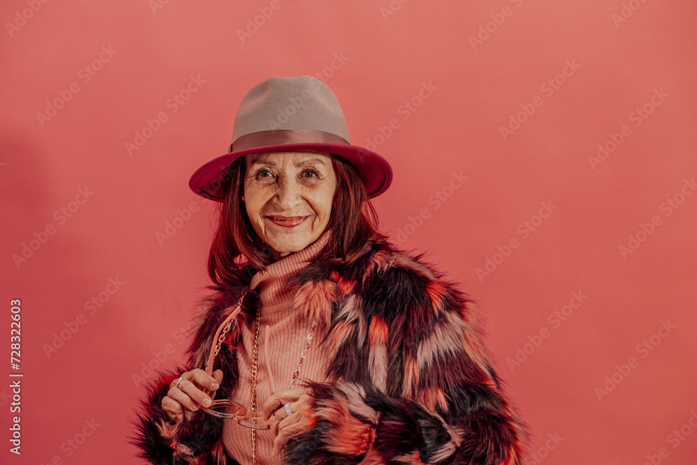 Happy senior woman wearing fur jacket in front of red wall Happy senior woman wearing fur jacket in front of red wall