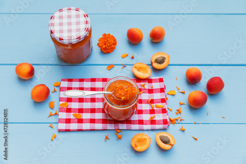 Homemade apricot jam with marigoldpetals and raw apricots on blue wood photo