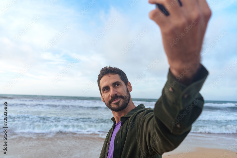 Man taking selfie through smart phone in front of sea at beach Man taking selfie through smart phone in front of sea at beach