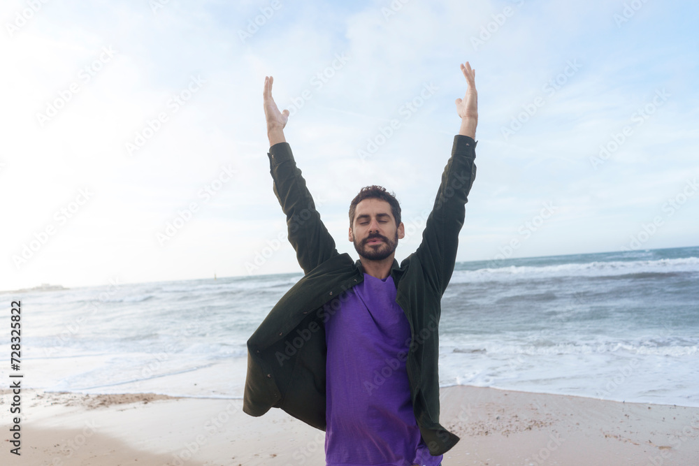 Carefree man standing with arms raised in front of sea at beach Carefree man standing with arms raised in front of sea at beach