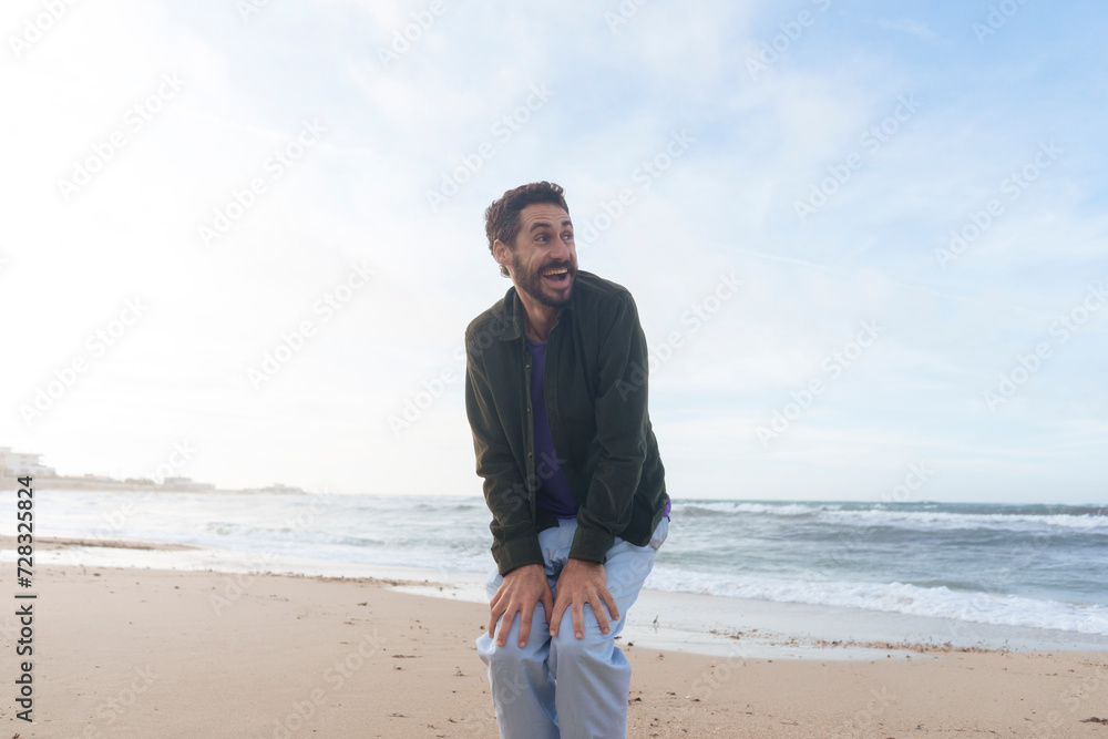 Cheerful man with hands on knees standing at beach Cheerful man with hands on knees standing at beach