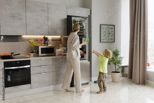 Woman standing near refrigerator with son in kitchen at home photo