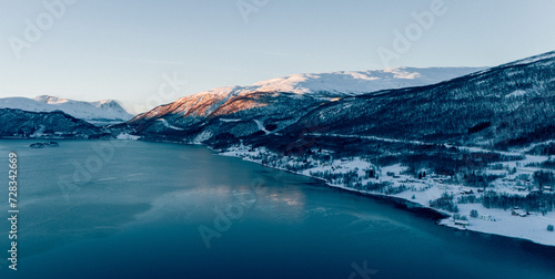 Aerial View over a Fjord in northern Norway during sunset with the sky reflecting in the water and the sun shining onto the peaks of the mountains