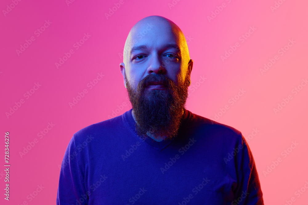 Portrait of bard bearded man in his 30s wearing blue sweater, looking at camera with calm face against pink background in neon light. Concept of human emotions, facial expression Portrait of bard bearded man in his 30s wearing blue sweater, looking at camera with calm face against pink background in neon light. Concept of human emotions, facial expression