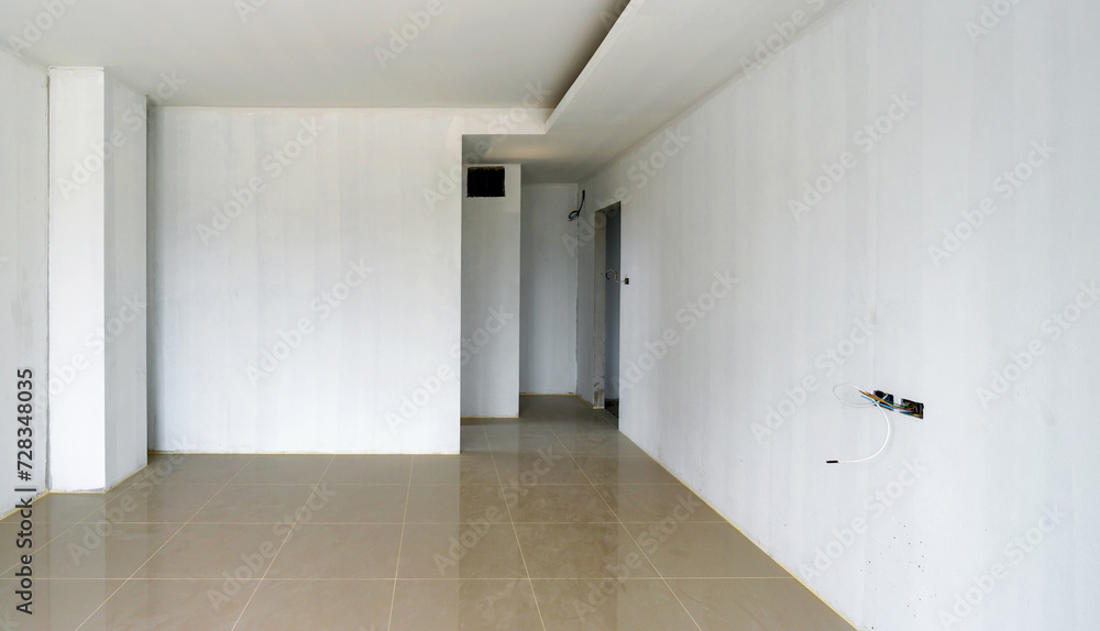 A bare white Primer color painted wall room with shiny marble tiled floor and lots of empty space. Unfinished room. Doors, service access panel and electrical outlet have not yet been installed. A bare white Primer color painted wall room with shiny marble tiled floor and lots of empty space. Unfinished room. Doors, service access panel and electrical outlet have not yet been installed.