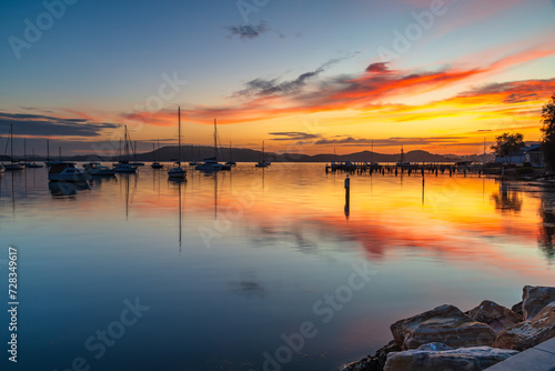 Sunrise with colourful cloud reflections and boats on the bay at Koolewong, NSW, Australia.