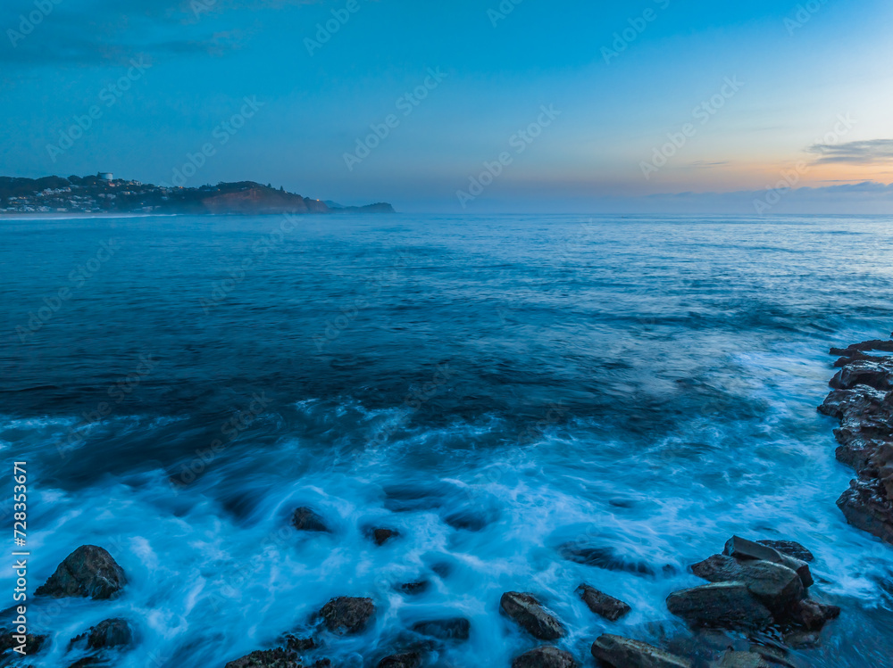 Sunrise over the calm ocean with light cloud and rocks