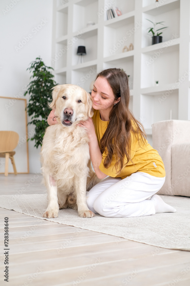 Portrait of happy young woman with pet dog, sitting on floor at home. Caucasian female hugging golden retriever in living room Portrait of happy young woman with pet dog, sitting on floor at home. Caucasian female hugging golden retriever in living room