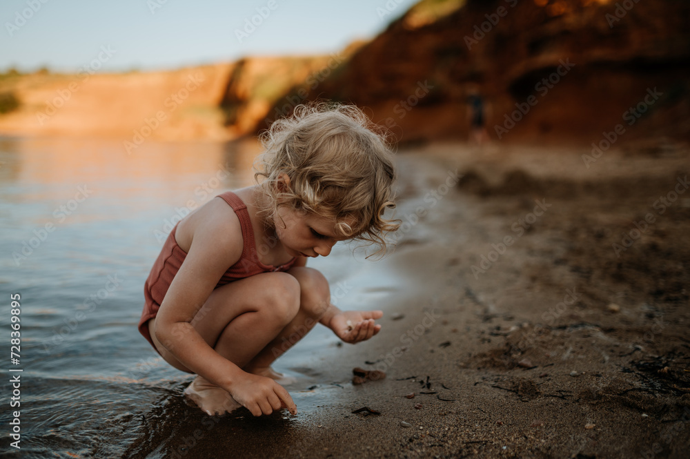 Small girl in swimsuit playing at beach, crouching, seraching for shells in the sand. Small girl in swimsuit playing at beach, crouching, seraching for shells in the sand.