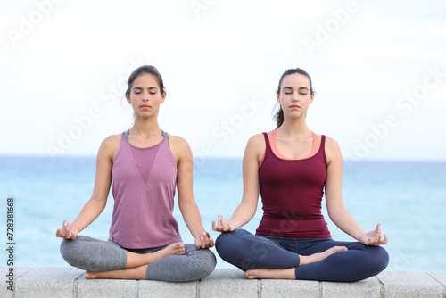 Two friends practicing yoga on the beach