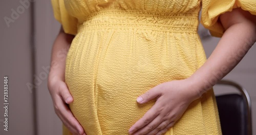 A pregnant woman caressing and stroking her own bulging baby bump with her hands in a circular motion. photo