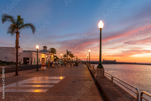 Obraz na płótnie Stroll the serene Arrecife promenade at dusk in Lanzarote, where palm silhouettes and a vibrant sunset create the perfect stock photo backdrop. w salonie
