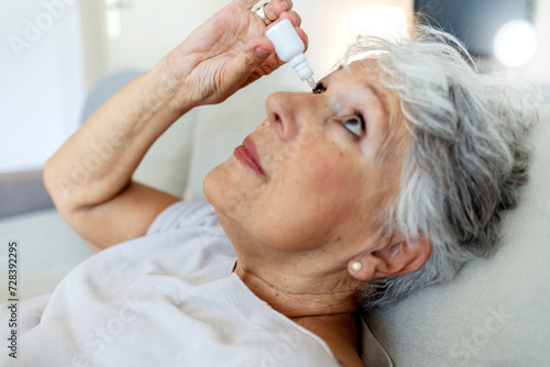 Old woman putting eye drop, closeup view of an elderly person using a bottle of eye drops in her eyes. A sick old woman suffering from irritated eyes, optical symptoms. Health concept.