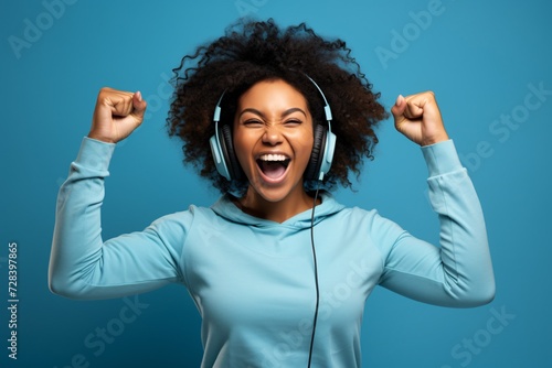 Ecstatic African American woman celebrates on blue studio background after winning online prize and receiving mobile promotion bonus.