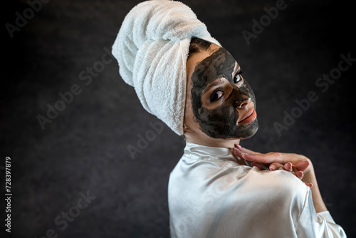 caucasian woman wear white towel with black clay mud nourishing mask on face isolated on black