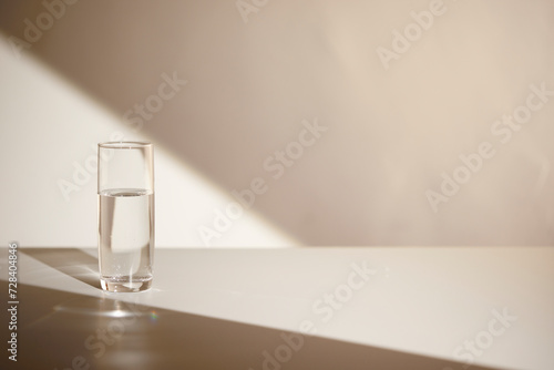 A water cup and shadow on a table in the sunlight.