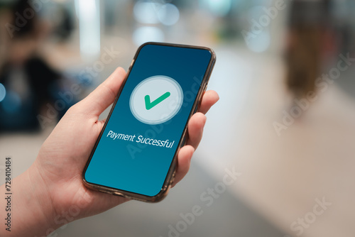 Digital online payment, online banking, online shopping and financial transaction success concept. Hand holding mobile phone and application showing payment successful message with green check mark. photo