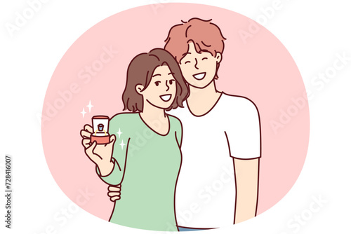 Young couple of man and woman stand in embrace and look at camera showing box with wedding ring. Bride and groom in casual clothes after proposal for joint family life. Flat vector illustration