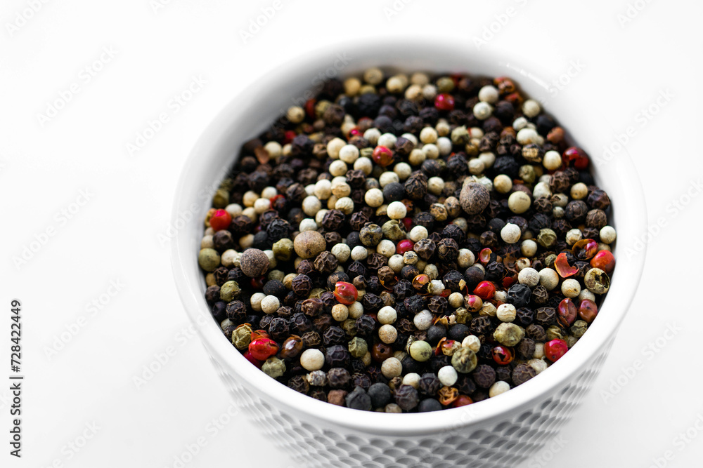 A mixture of pepper varieties with peas on the white plate on the white background. Heap of various pepper. Mix of red, black and white peppercorn seeds isolated on white. Top view A mixture of pepper varieties with peas on the white plate on the white background. Heap of various pepper. Mix of red, black and white peppercorn seeds isolated on white. Top view