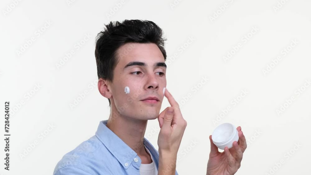 Close up portrait of smiling Caucasian young man applying facial cream, isolated on white background. Skin care, man beauty, using cosmetic, skin wellbeing, cosmetology concept. Close up portrait of smiling Caucasian young man applying facial cream, isolated on white background. Skin care, man beauty, using cosmetic, skin wellbeing, cosmetology concept.
