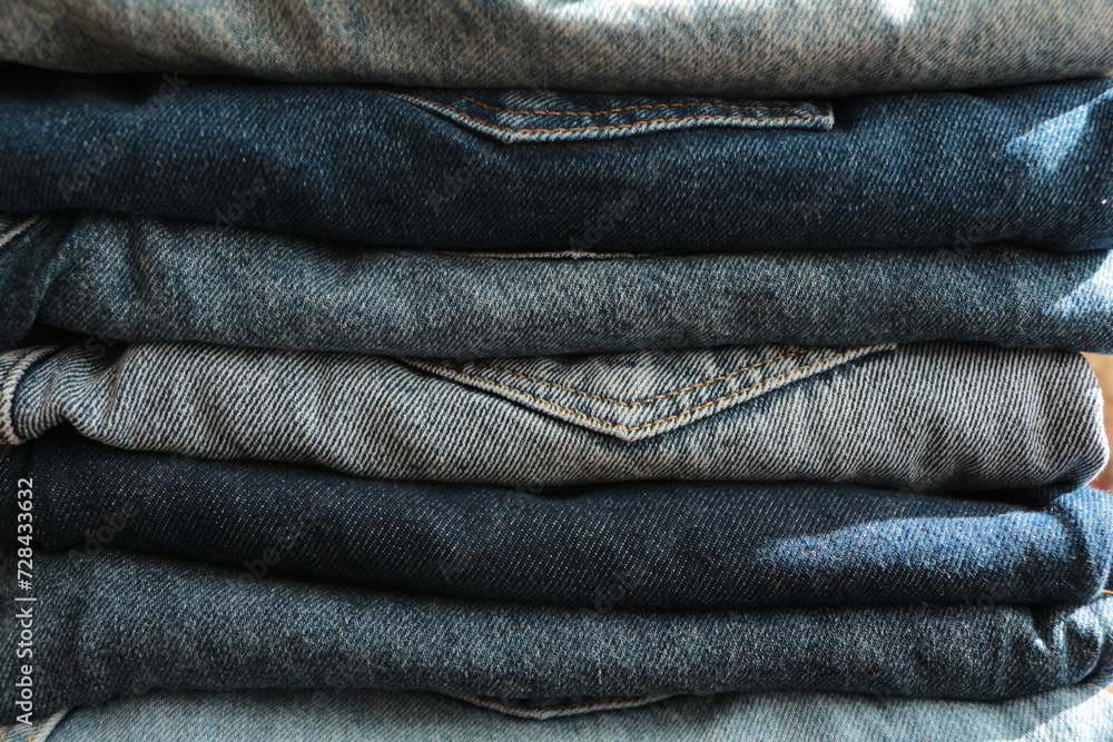 Close up the Stack of jeans in different shades of blue. Folded denim jeans pants, different shades of denim jeans in a row. Denim texture or denim jeans background. Close up the Stack of jeans in different shades of blue. Folded denim jeans pants, different shades of denim jeans in a row. Denim texture or denim jeans background.
