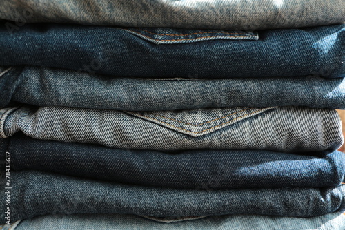 Close up the Stack of jeans in different shades of blue. Folded denim jeans pants, different shades of denim jeans in a row. Denim texture or denim jeans background.