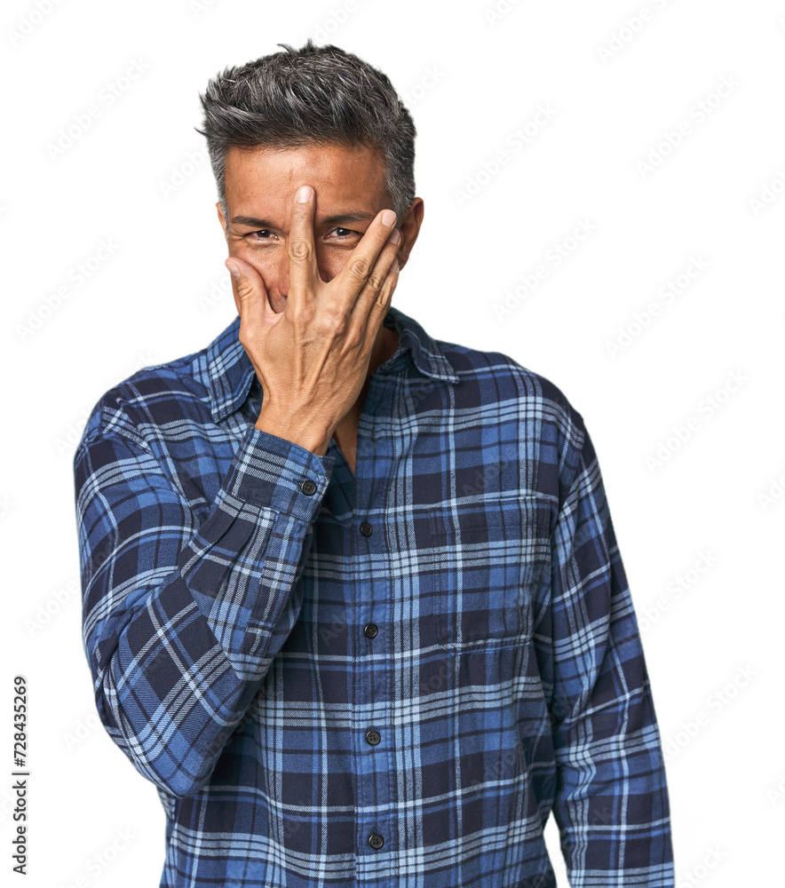 Middle-aged Latino man blink at the camera through fingers, embarrassed covering face. Middle-aged Latino man blink at the camera through fingers, embarrassed covering face.