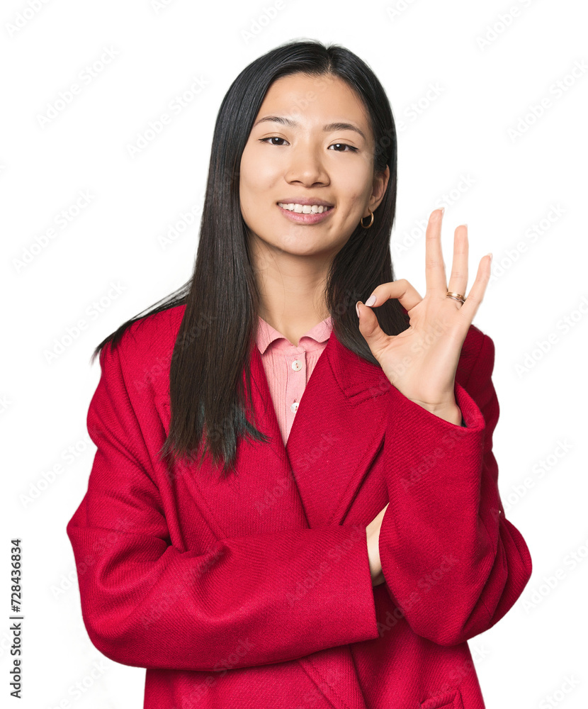 Young Chinese woman in studio setting winks an eye and holds an okay gesture with hand. Young Chinese woman in studio setting winks an eye and holds an okay gesture with hand.
