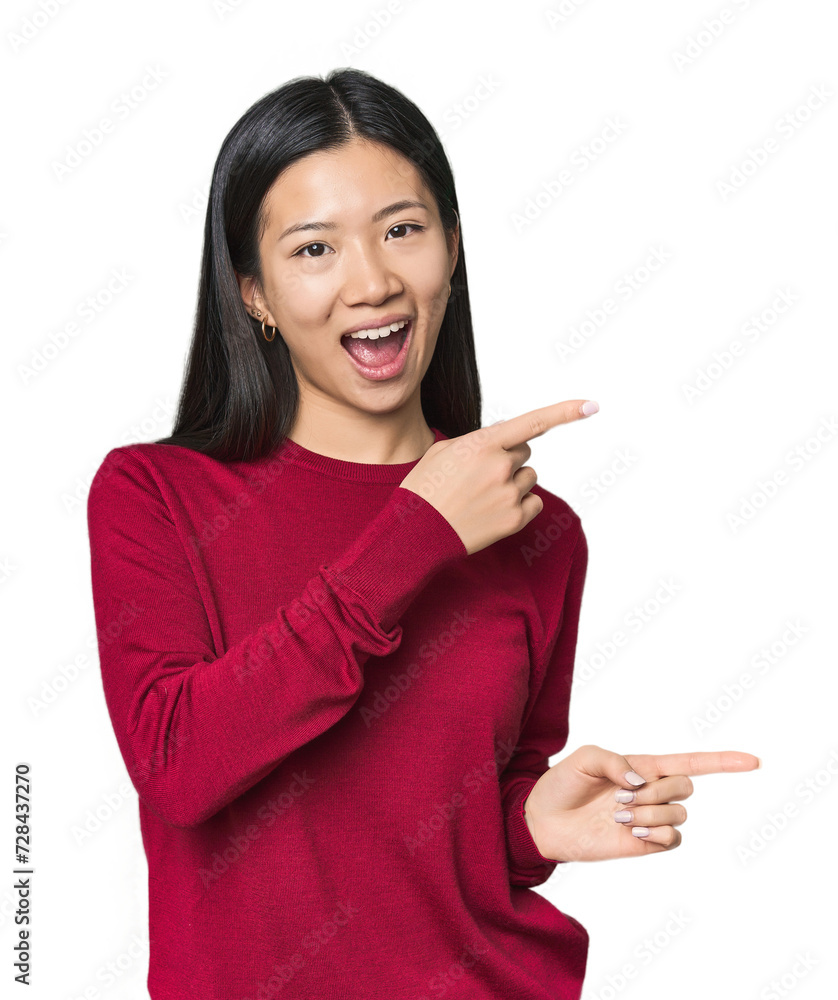 Young Chinese woman in studio setting pointing with forefingers to a copy space, expressing excitement and desire. Young Chinese woman in studio setting pointing with forefingers to a copy space, expressing excitement and desire.