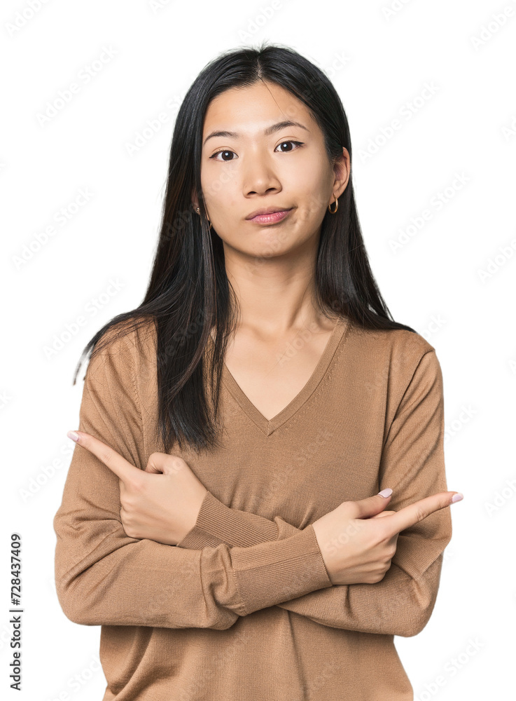 Young Chinese woman in studio setting points sideways, is trying to choose between two options. Young Chinese woman in studio setting points sideways, is trying to choose between two options.