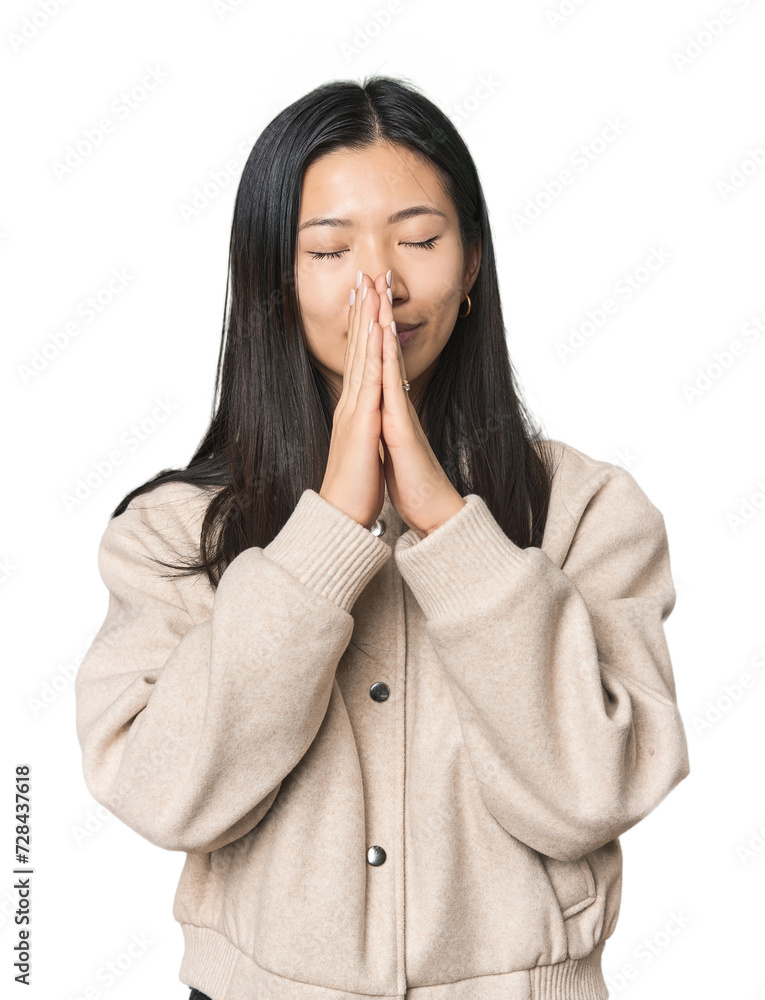 Young Chinese woman in studio setting holding hands in pray near mouth, feels confident. Young Chinese woman in studio setting holding hands in pray near mouth, feels confident.