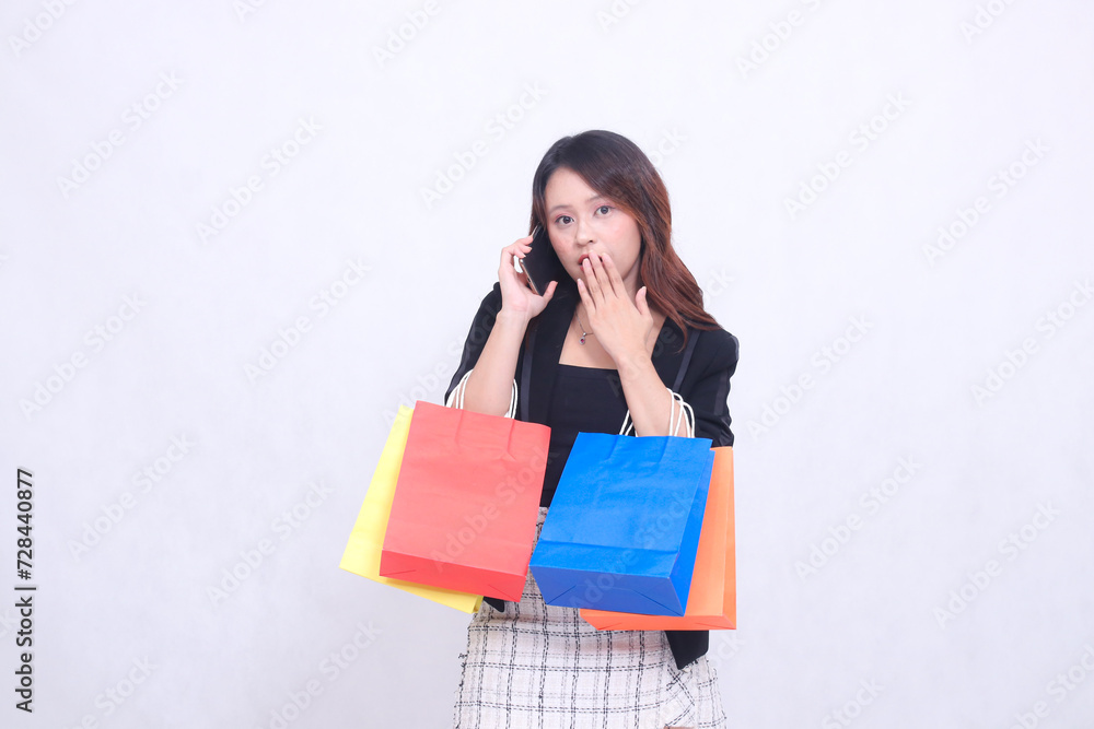 Beautiful Asian girl 20s formal office customer shocked by telephone looking at camera while carrying shopping paper bag isolated on white background Beautiful Asian girl 20s formal office customer shocked by telephone looking at camera while carrying shopping paper bag isolated on white background