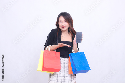 customer beautiful asian girl 20s formal office smile introduces cell phone gadget while carrying shopping paper bag isolated white background