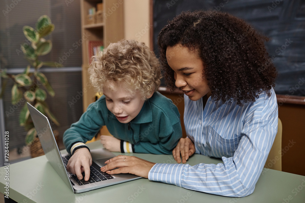 Portrait of young Black female teacher with little boy using laptop computer in school classroom Portrait of young Black female teacher with little boy using laptop computer in school classroom