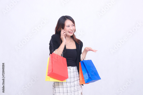 Beautiful Asian girl customer 20s formal office smiling laughing while calling hand to the side lower left while carrying shopping paper bag isolated white background