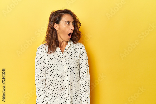 Middle-aged woman on a yellow backdrop being shocked because of something she has seen. photo