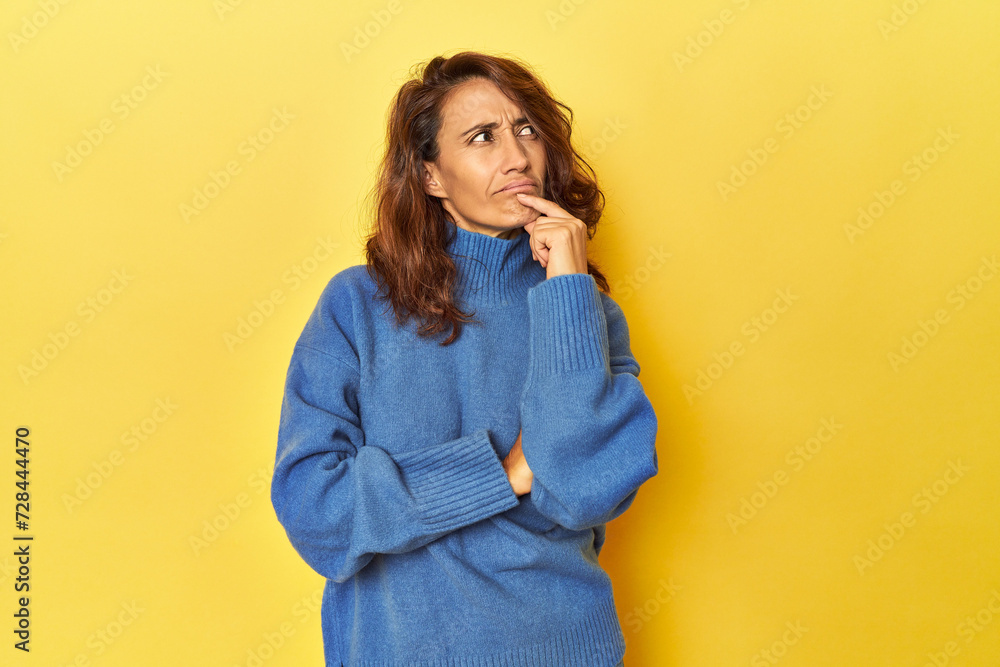 Middle-aged woman on a yellow backdrop thinking and looking up, being reflective, contemplating, having a fantasy. Middle-aged woman on a yellow backdrop thinking and looking up, being reflective, contemplating, having a fantasy.