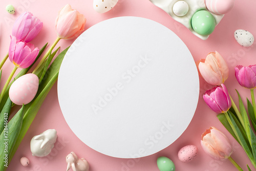 Spring Spectacle: top view delightful arrangement of vibrant eggs, cute bunnies, blooming tulips on pastel pink surface. Empty circle serves as canvas for text or adverts, capturing Easter April mood
