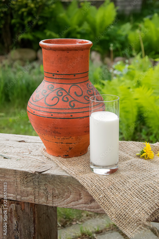 A glass of milk next to a clay jug in patterns. Country style. Summer. A glass of milk next to a clay jug in patterns. Country style. Summer.