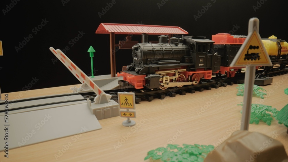Model of a children's plastic steam train with freight cars stands on the tracks at a railroad station. The atmosphere is ideal for use in children's presentations or toy advertising.