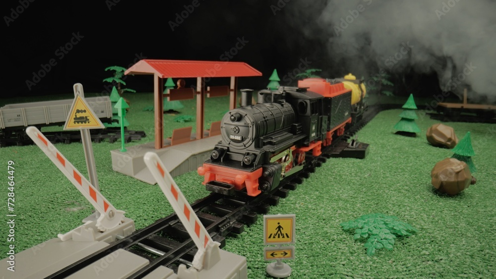 Model of a children's plastic steam train with freight cars and ferry rides along the tracks and arrives at the platform. Atmosphere is ideal for use in children's presentations or toy advertising.