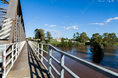 Footpath on side of bridge overlooking brown floodwaters or raging river