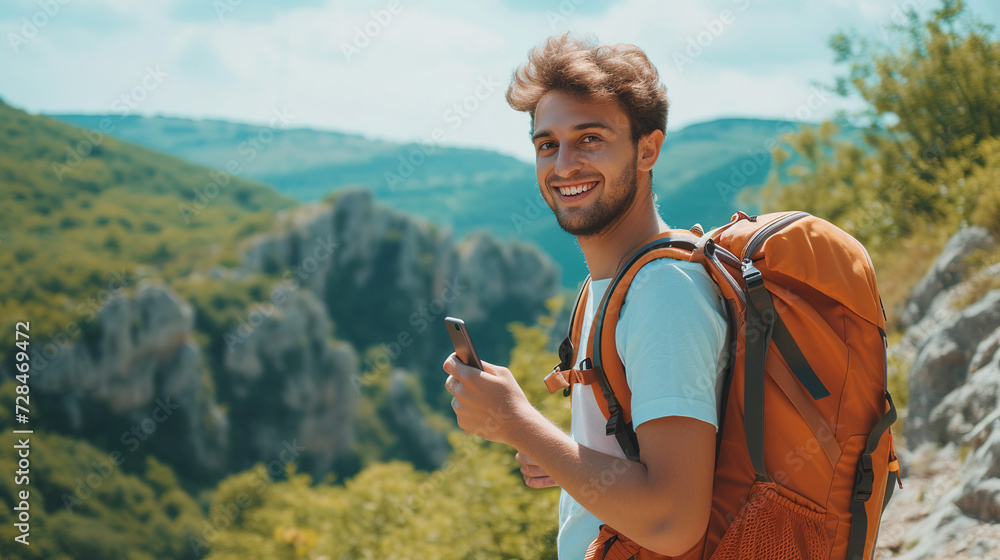 A young cheerful male traveler carries a backpack with things, uses a phone, a smartphone. A tourist leads an active healthy lifestyle, uses mobile Internet while hiking
