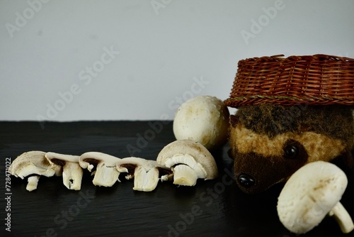 champignons lie on a black background, and next to them a hedgehog covered with a wicker basket