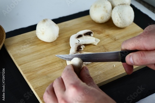 Male hands cutting champignons on a wooden board
