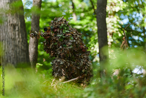 A highly skilled elite sniper, camouflaged in the dense forest, stealthily maneuvers through dangerous woodland terrain on a covert and precise mission photo