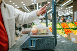 The man's finger selects the desired product in the supermarket on the touch screen of the electronic scale. Person weighing a bag of apples at a supermarket checkout counter. 
